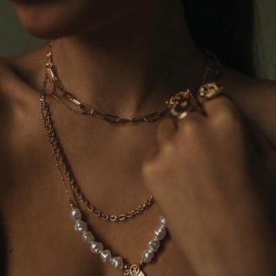 Mulher a usar colares dourados e colar de pérolas com pendente