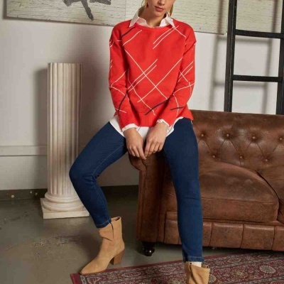 Mulher com camisola vermelha, jeans azuis e botas castanhas sentada em sofá de couro