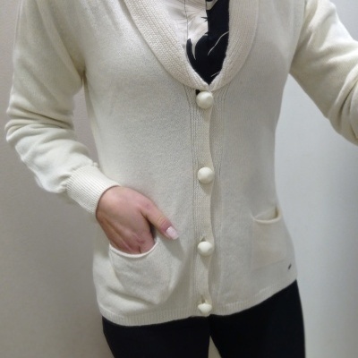 Camisola de malha creme com botões e bolsos, sobre camisa preta e branca, com calças pretas