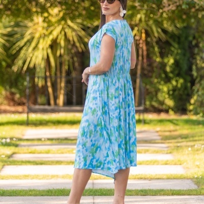 Mulher de costas com vestido azul e verde, salto alto transparente, ao ar livre