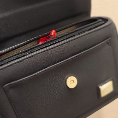 Carteira preta com fecho dourado e puxador de zíper vermelho aberta