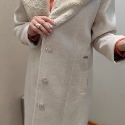 Casaco bege com gola de pelo, botões brilhantes, usado por pessoa com camisa laranja e anéis