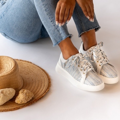 Ténis azuis e brancos com atacadores ao lado de chapéu de palha e pedras