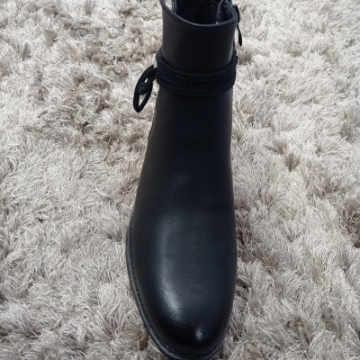 Bota preta em pele com sola e cadarço preto sobre tapete bege peludo