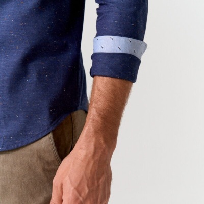 Braço e tronco de pessoa com camisa azul escura com pontos coloridos e calças castanhas, manga dobrada mostrando forro azul claro com padrão.