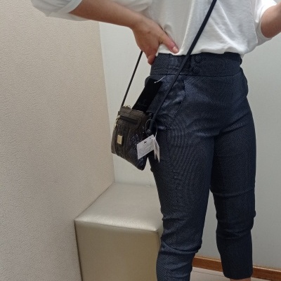 Pessoa vestindo blusa branca, calças azul escuro, sapatos pretos de salto alto e bolsa preta pequena num ambiente interior.