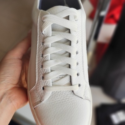 Ténis branco em pele sintética visto de cima, segurado por uma mão