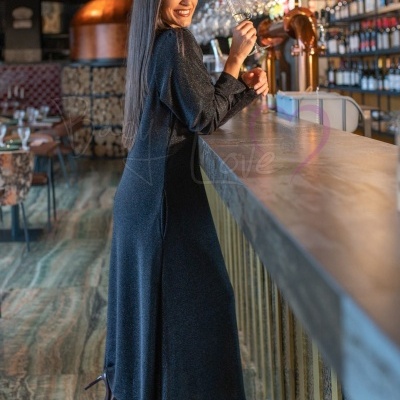 Mulher de vestido preto longo de mangas compridas num bar com copo de vinho.