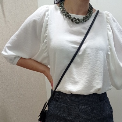 Pessoa vestindo blusa branca de manga bufante com colar grosso e mala preta de tiracolo