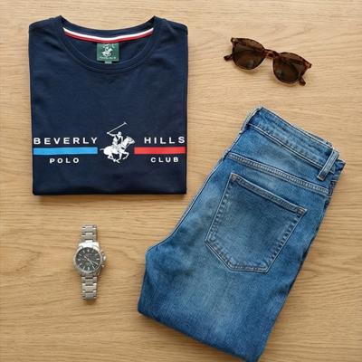 Conjunto de t-shirt azul-marinho, jeans azuis, óculos de sol castanhos e relógio de metal sobre madeira.