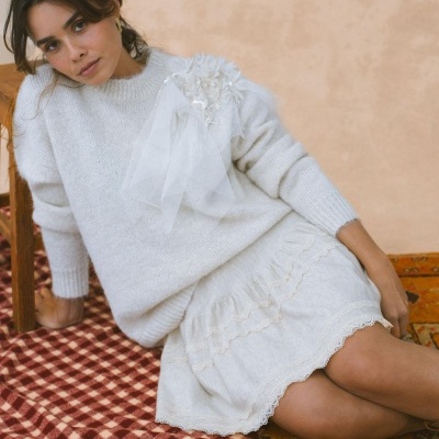 Mulher vestindo camisola e saia brancas, sentada em tapetes de padrões diferentes