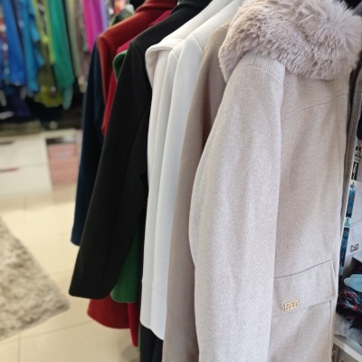 Casacos de inverno em cores variadas pendurados numa loja, destaque para casaco bege com gola de pelo.
