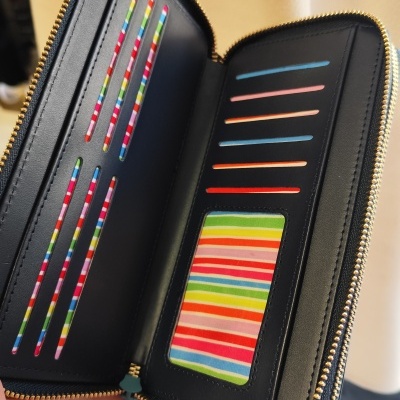 Carteira preta com fecho de zip dourado e compartimentos coloridos para cartões