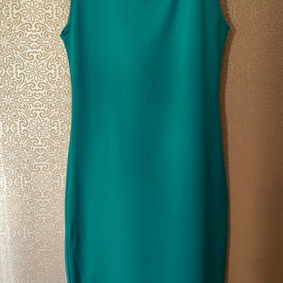 Vestido verde turquesa pendurado num cabide preto contra parede bege decorativa