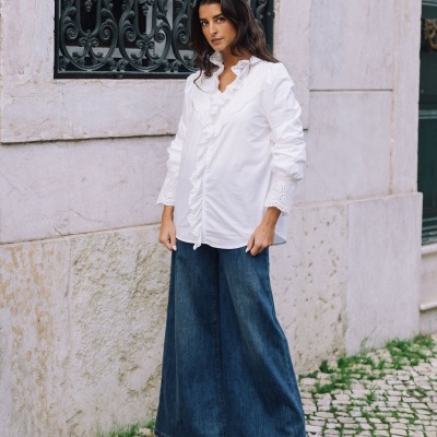 Mulher vestindo calças largas de ganga azul e camisa branca com detalhes em ambiente urbano exterior