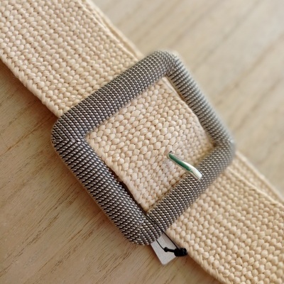 Cinto bege de tecido com fivela metálica texturada sobre madeira clara