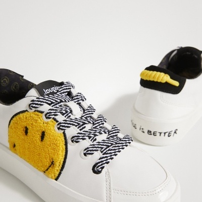 Ténis brancos com smiley amarelo felpudo e texto 'LIFE IS BETTER' no calcanhar