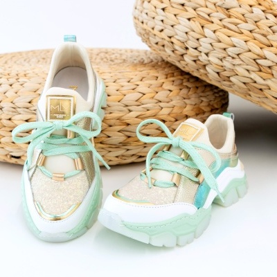 Sapatilhas verdes menta com detalhes dourados e brancos colocadas sobre superfície branca com objetos de palha ao fundo