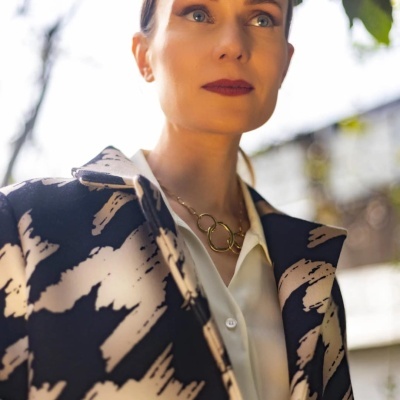 Mulher com casaco blazer preto e creme, camisa branca e colar dourado ao ar livre