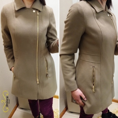 Casaco bege de mulher com fecho e bolsos dourados em ambiente interior