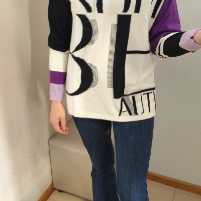 Camisola colorblock preta, branca, roxa e lilás com letras pretas, calças jeans azuis e sapatos castanhos