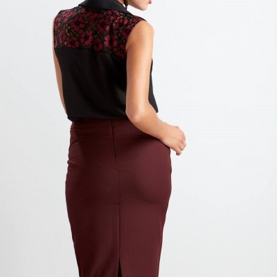 Mulher de costas com blusa preta e detalhe floral vermelho e saia lápis bordô com racha