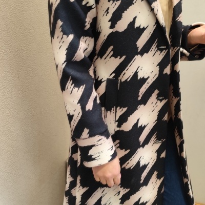 Casaco comprido preto e bege padrão abstrato, usado com camisa bege e jeans azuis.