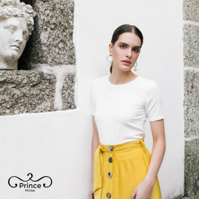 Mulher com t-shirt branca e saia amarela perto de parede com escultura em pedra