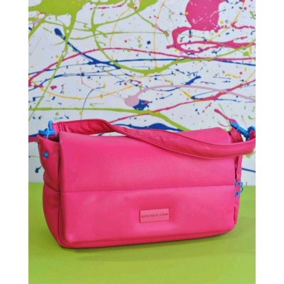 Bolsa cor-de-rosa com alça azul sobre superfície verde e parede colorida ao fundo