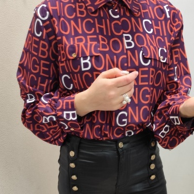 Blusa roxa com letras laranja e branca combinada com calças pretas de tecido brilhante e botões dourados