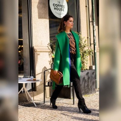 Mulher com casaco verde a andar na rua em frente a café