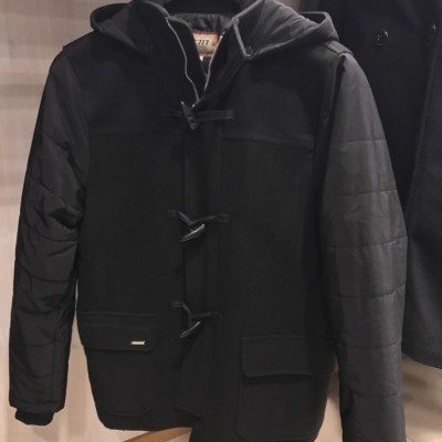 Casaco preto com capuz, mangas acolchoadas, botões alamares, dois bolsos com aba, pendurado em cabide