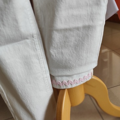 Calças brancas com bordado rosa na bainha apoiadas em cadeira de madeira