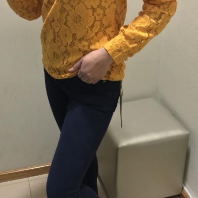 Blusa de renda amarela, calças azul-escuro e sapatilhas brancas em ambiente interior