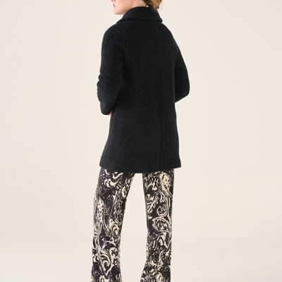 Mulher vista de costas a usar casaco preto, calças estampadas e sapatos pretos.