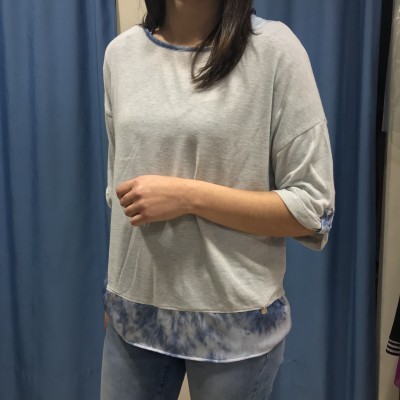 Mulher com camisola cinza clara com detalhes azuis tie-dye nas mangas e bainhas