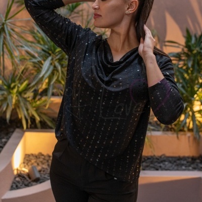 Mulher com blusa preta com círculos brilhantes e calças pretas em ambiente exterior com plantas