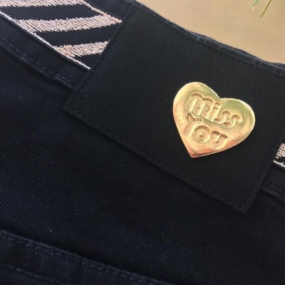 Calças pretas com botão dourado em forma de coração e cinto preto e branco