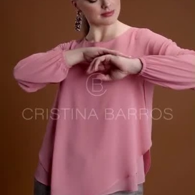 Mulher a usar blusa rosa e calças xadrez cinzentas com fundo castanho e texto CRISTINA BARROS.