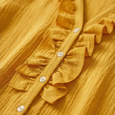 Detalhe de blusa amarela com botões e folhos