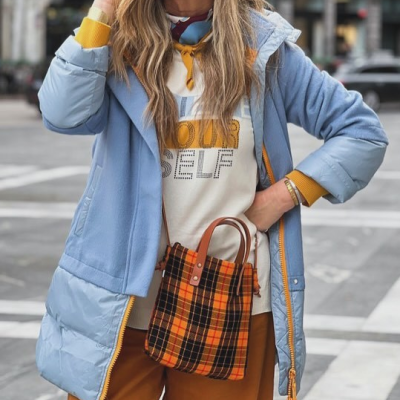 Pessoa com casaco azul e mala xadrez laranja a preto em ambiente urbano