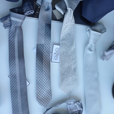 Gravatas e gravata borboleta cinza e azul com padrões numa superfície branca