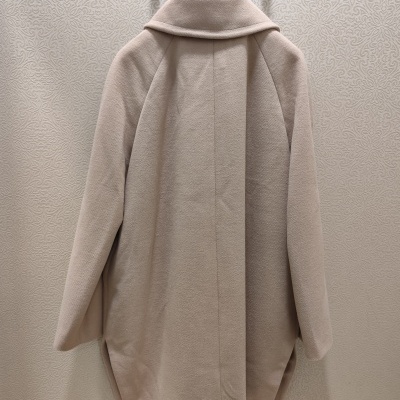 Casaco bege claro pendurado de costas com papel de parede decorativo ao fundo.