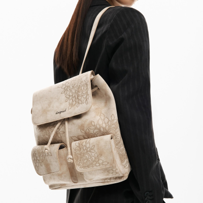 Mochila bege com bordados florais e bolsos frontais, usada por mulher de blazer preto.