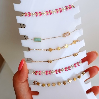 Expositor branco com sete pulseiras coloridas e douradas segurado por mão com unhas pintadas de rosa