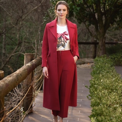 Mulher a usar casaco comprido e calças vermelhas com top branco estampado em passadiço exterior.