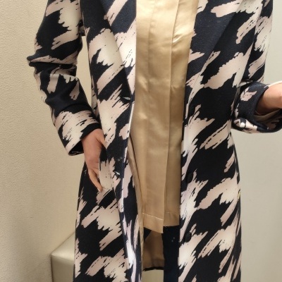 Casaco comprido com padrão abstrato preto e bege sobre camisa bege e calças azuis