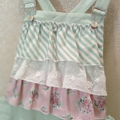 Vestido infantil com alças verdes e camadas de tecido em riscas, floral e bordado