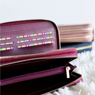 Carteira vinho com fecho dourado e interior colorido sobre superfície branca felpuda