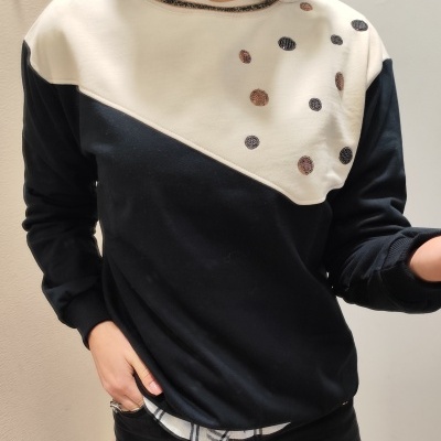 Sweatshirt branco e preto com bordados redondos em tons castanhos e pretos, usada por mulher.